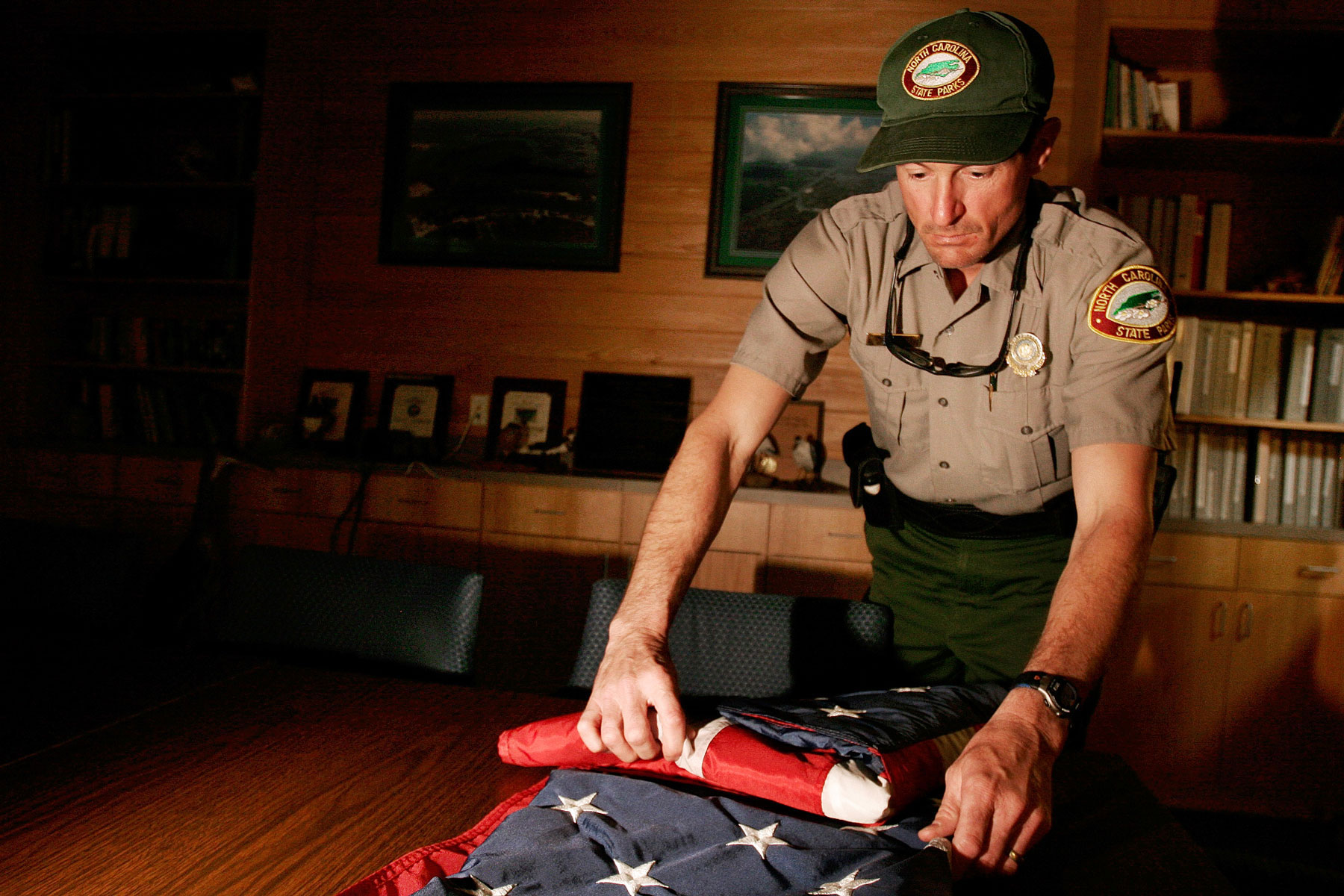 A man in a state park uniform folds an American flag