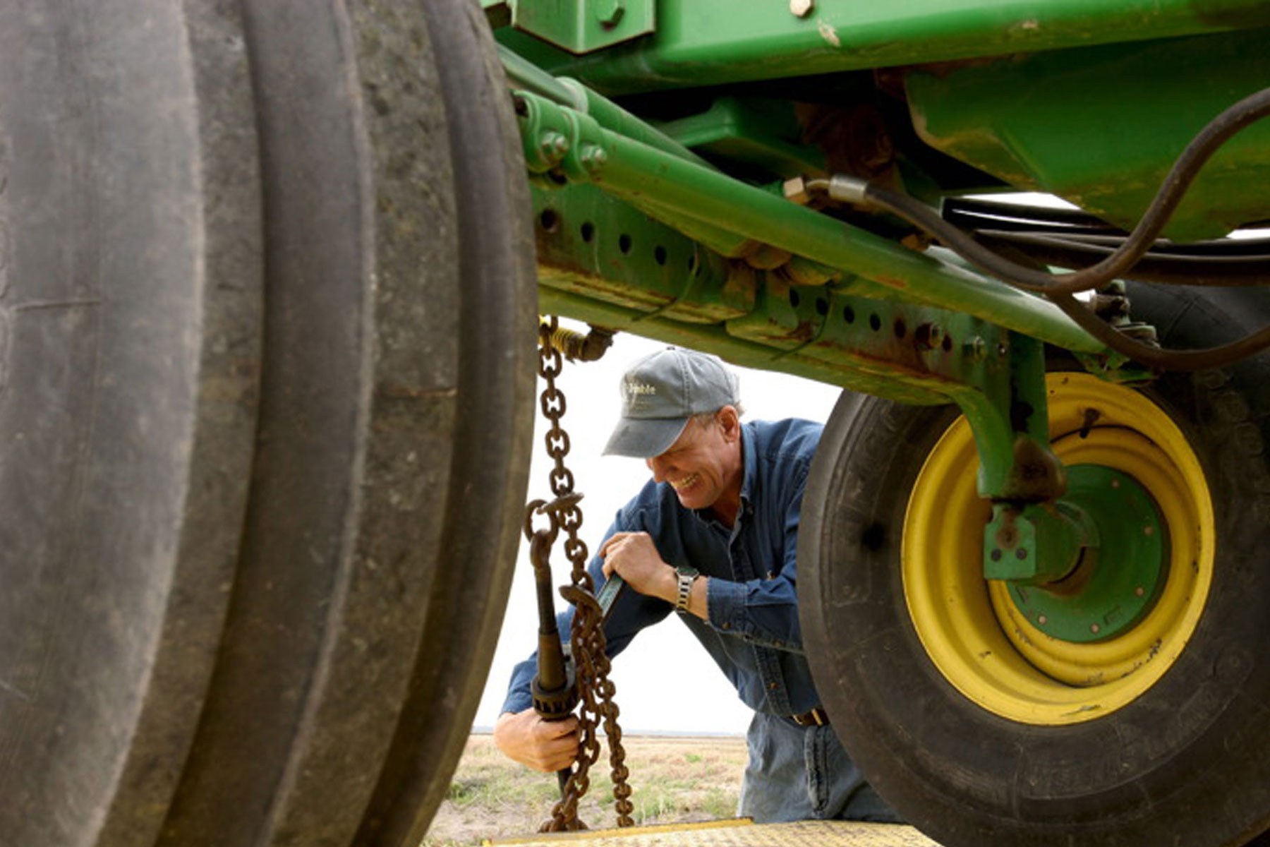 A man uses a wrench while working on the underside of a tractor