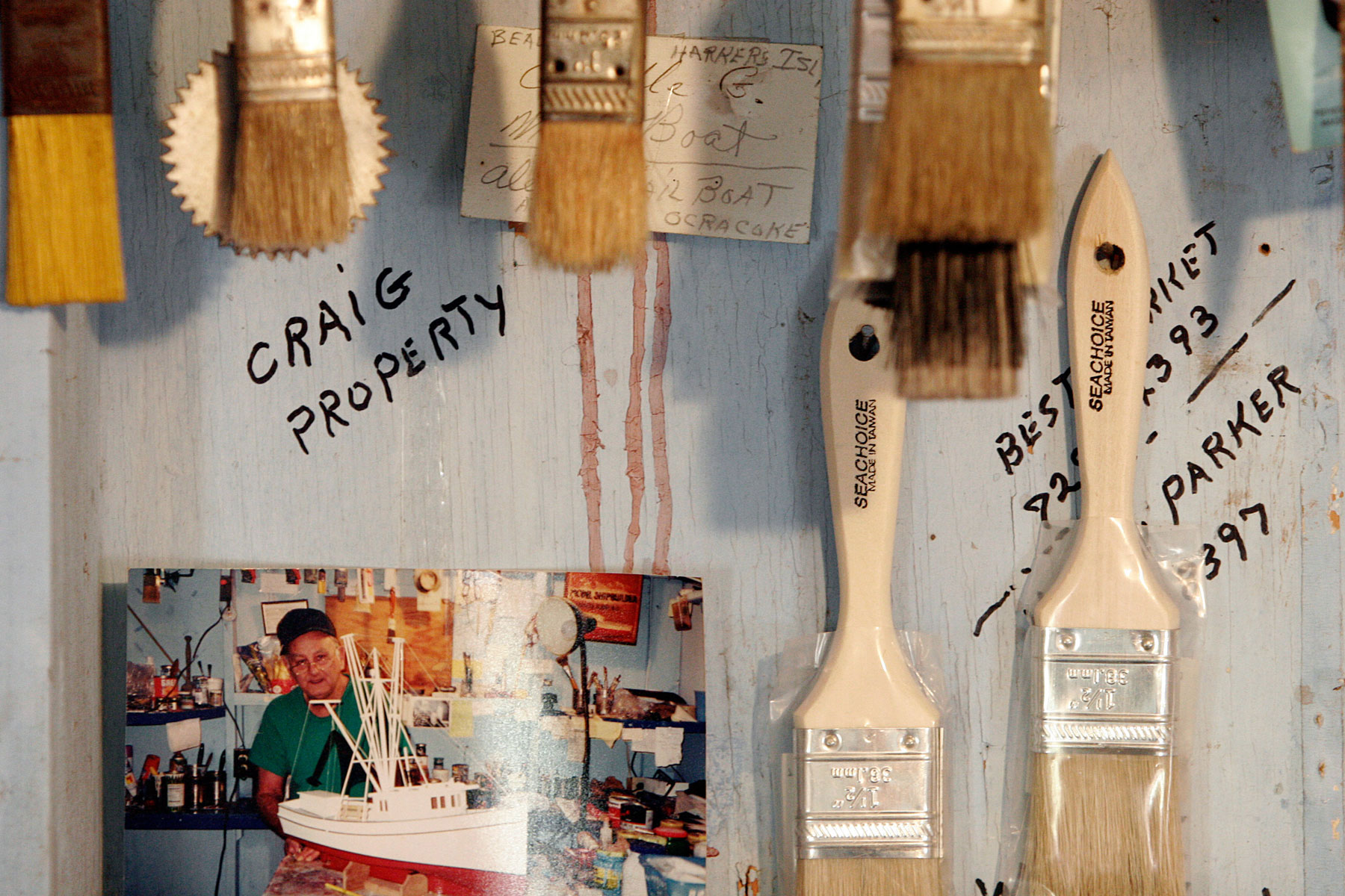 Painbrushes hanging on a weathered wall, along with a photograph of a man and a boat