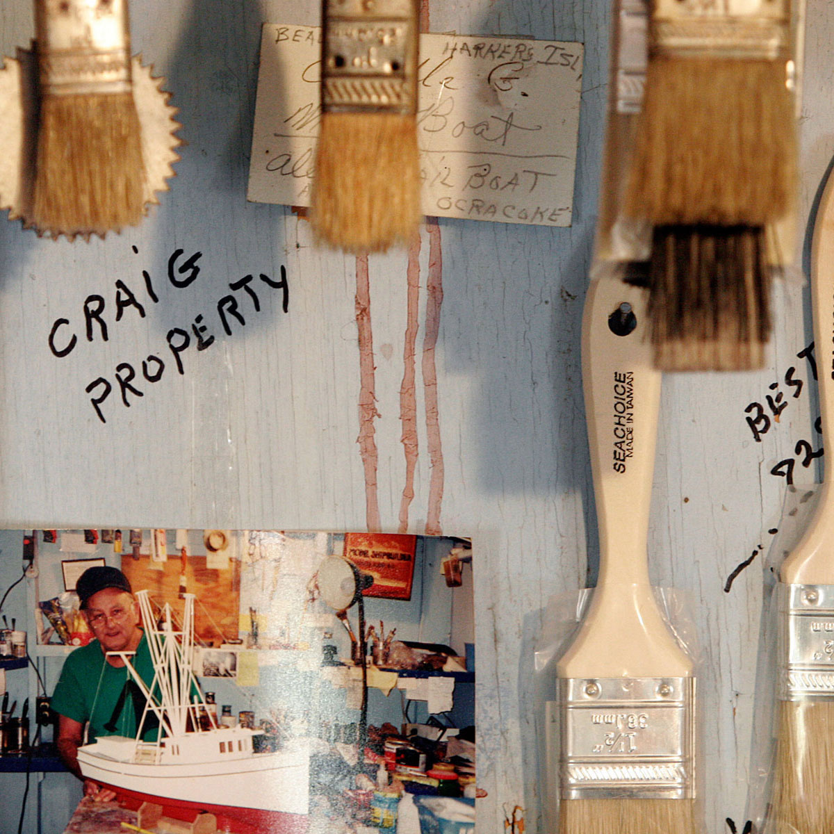 Painbrushes hanging on a weathered wall, along with a photograph of a man and a boat