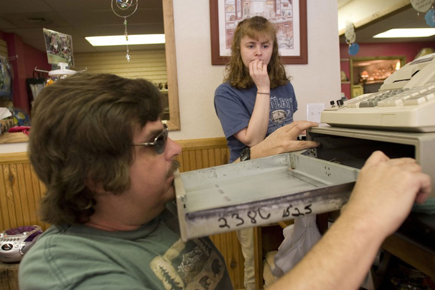 A man in sunglasses props open a drawer with his chin while a woman looks on with concern