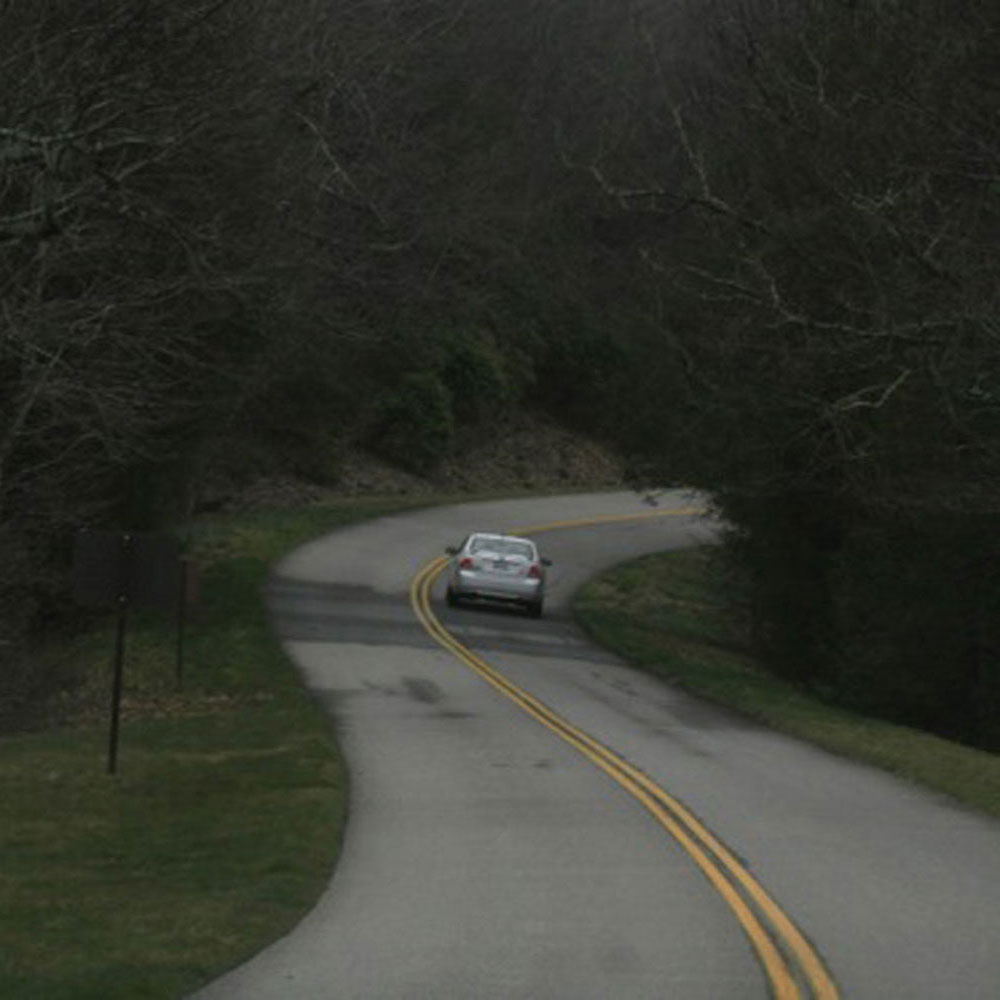A gray car drives away from the camera on a winding road