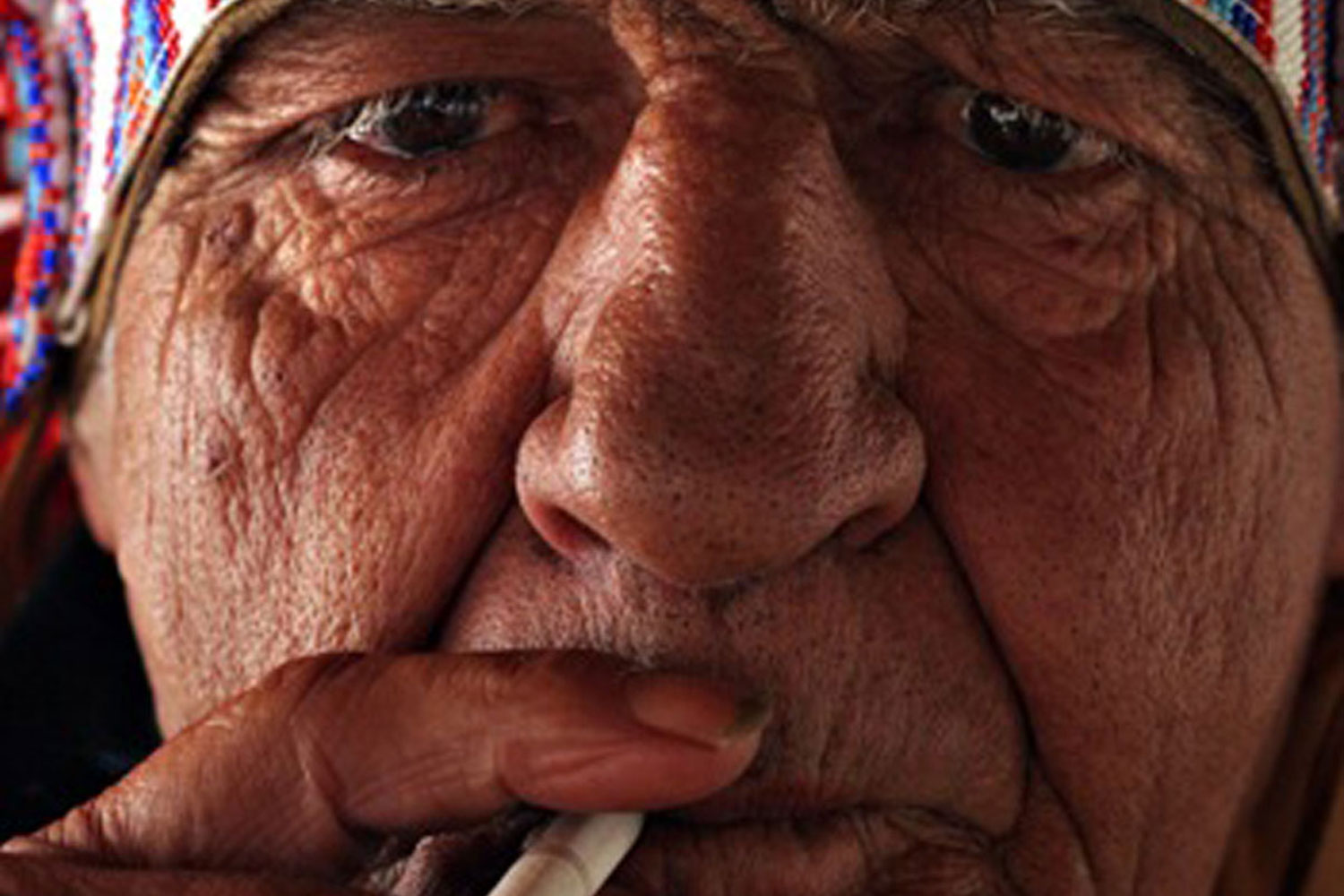A close up of a wrinkled man smoking a cigarette