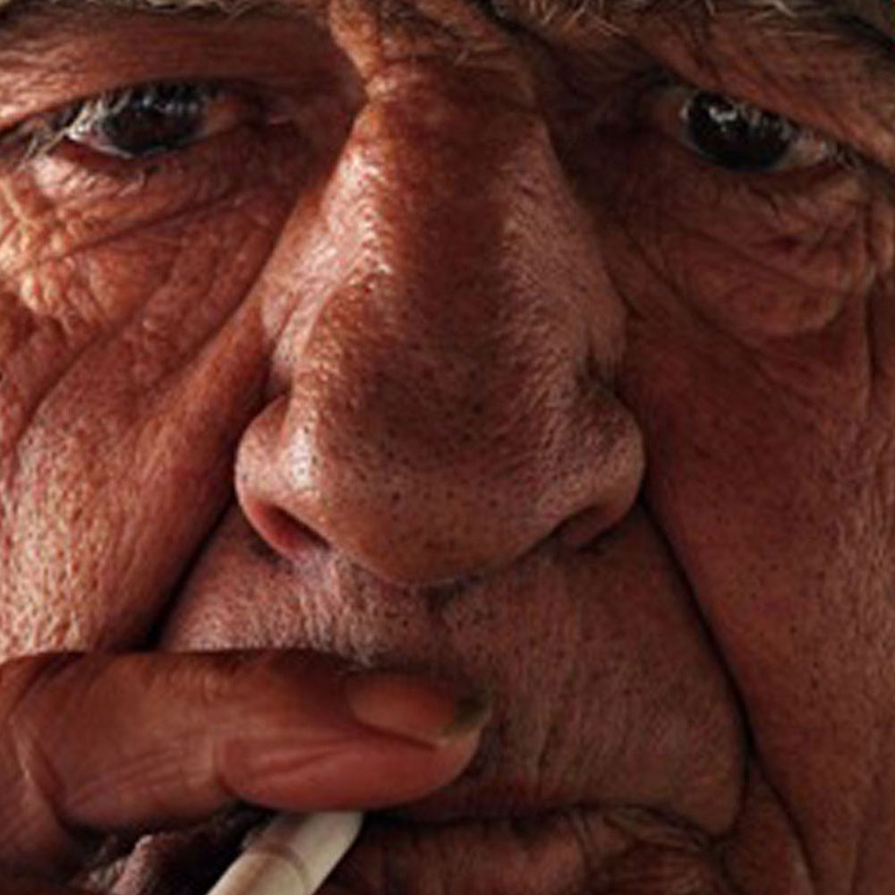 A close up of a wrinkled man smoking a cigarette
