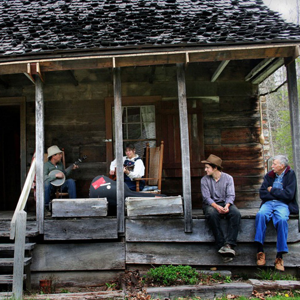 A group of musicians play on the porch of an old wooden house