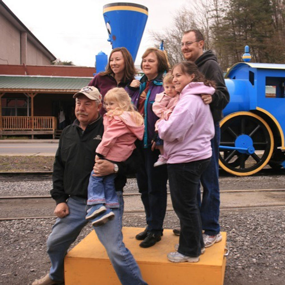 A family of seven poses for a picture in front of a blue steam engine