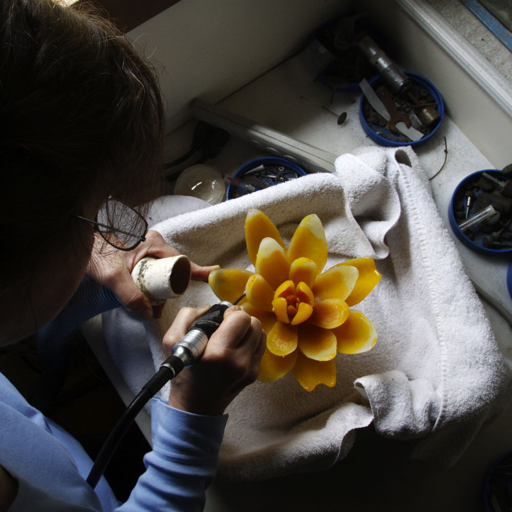 A woman works on a glass flower sculpture