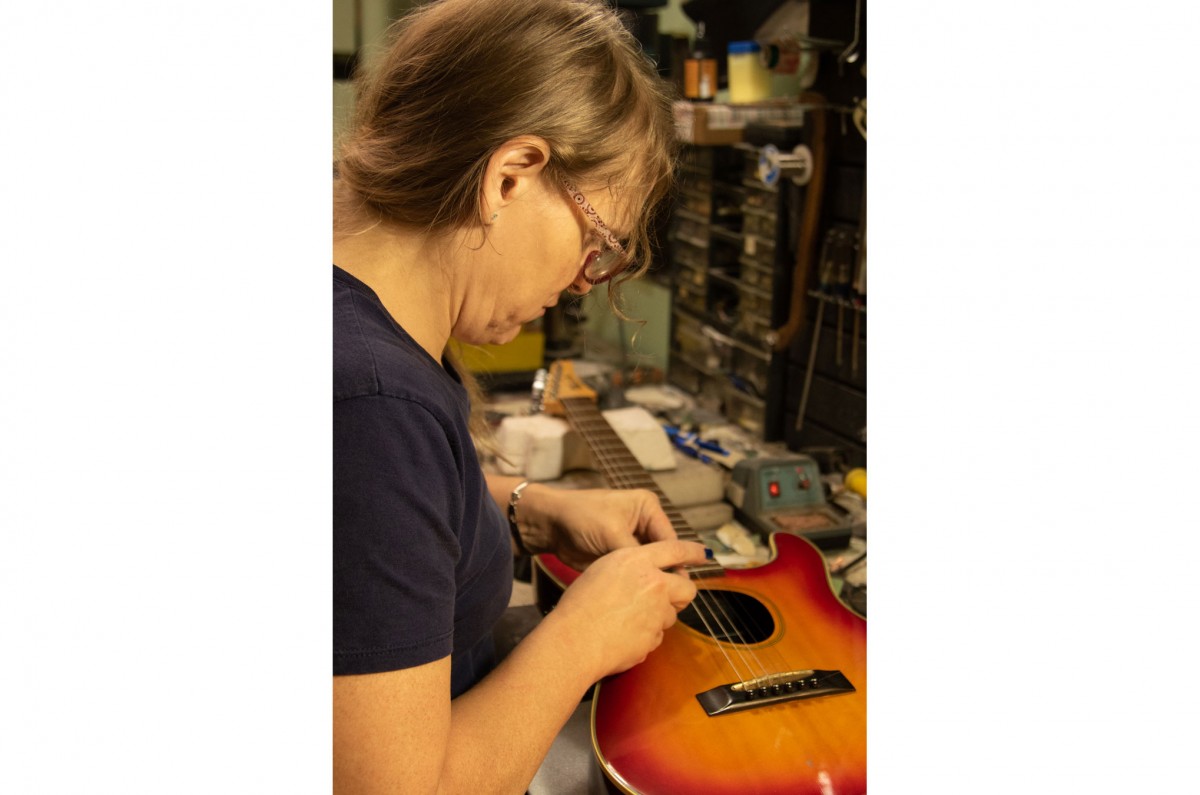 Samantha begins to replace the pickups on the guitar so that it can be used with an amplifier.