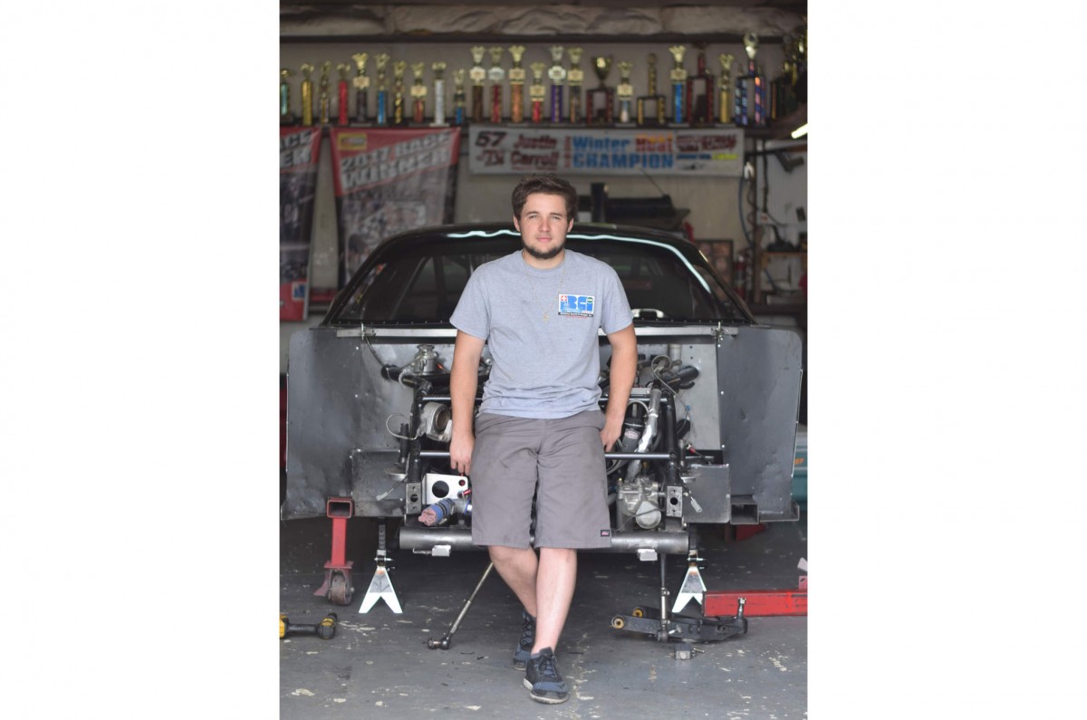 Racer Justin Carroll stands with one of his two race cars in front of his trophy display in his shop behind his home in Concord, North Carolina.