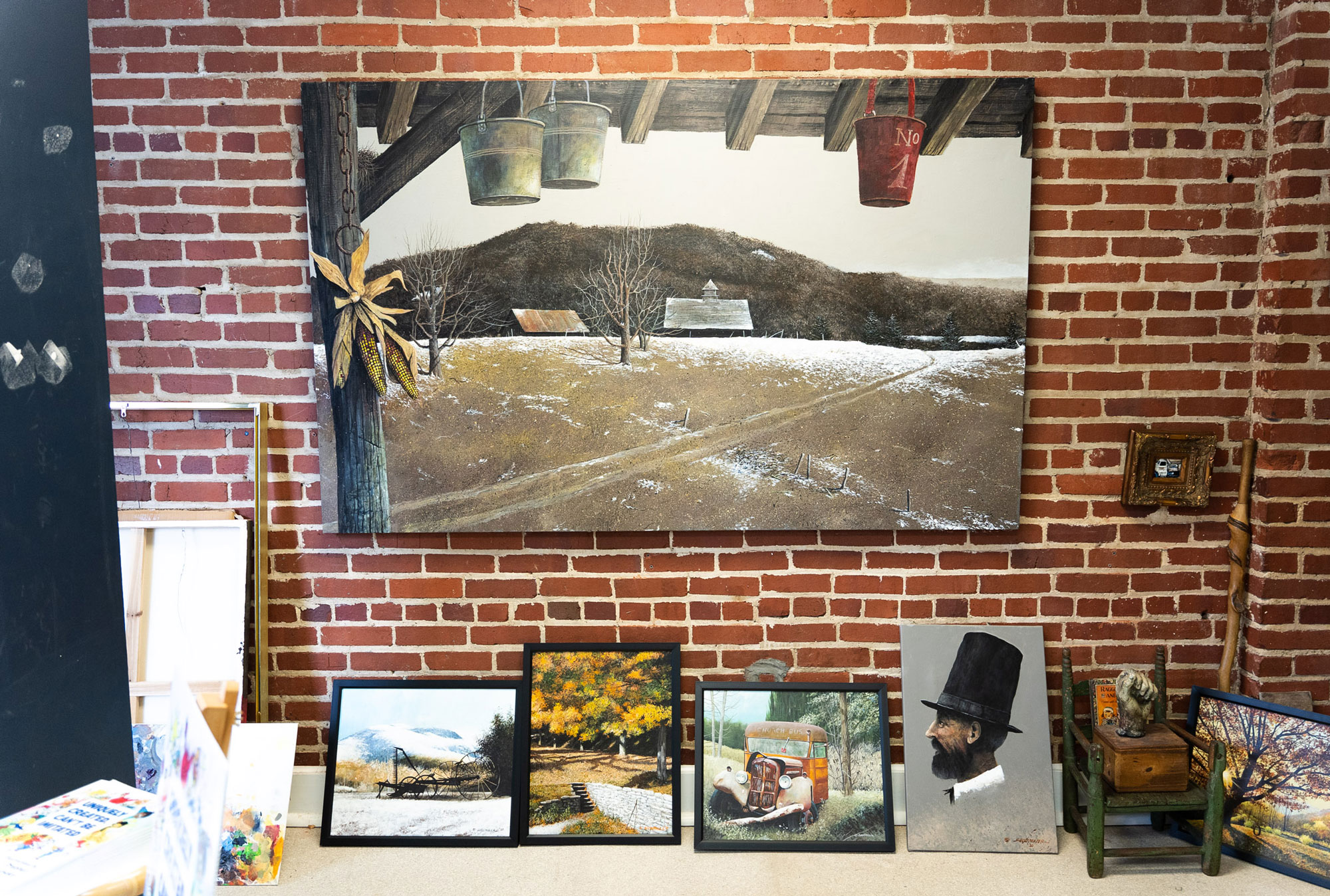 A series of paints are displayed on a wall and on a table, showing fall and winter scenes