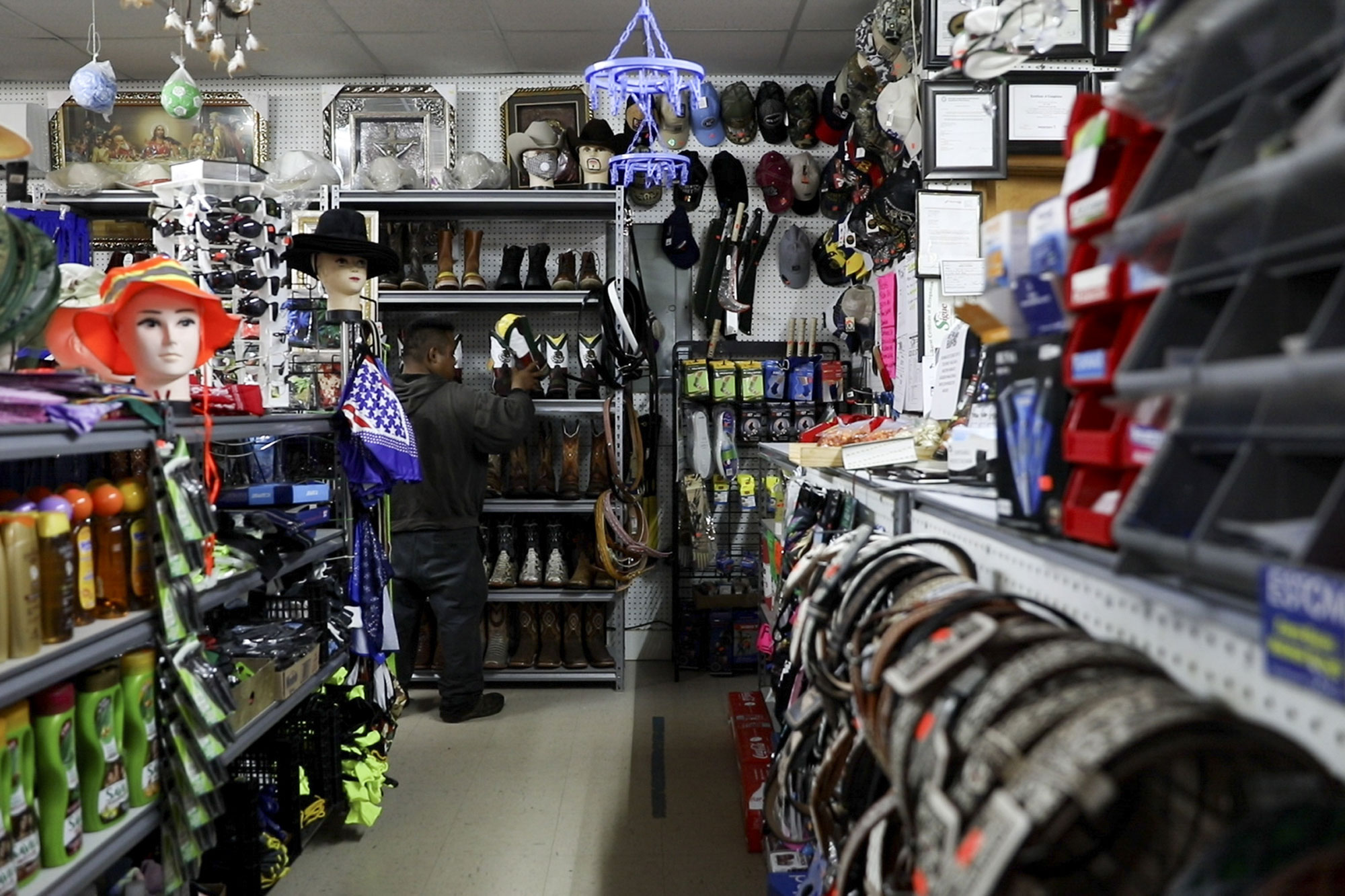 A man stands in the background of a supply shop with hats, boots, and belts