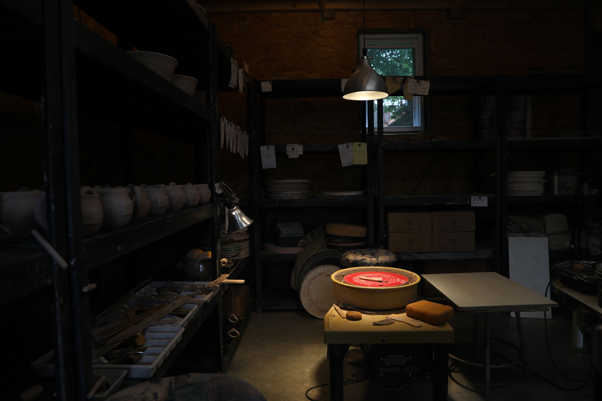 A darkened pottery studio with a wheel and pots on a shelf