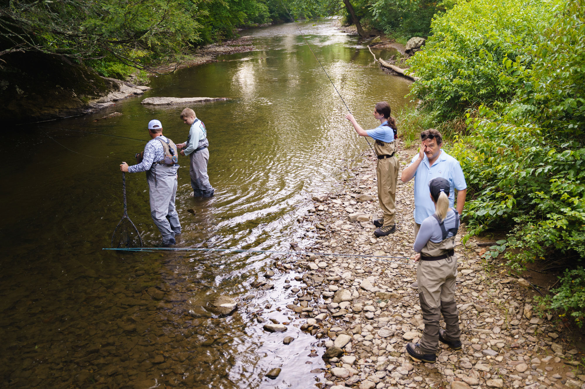 A group stands in and around a river casting their fishing lines
