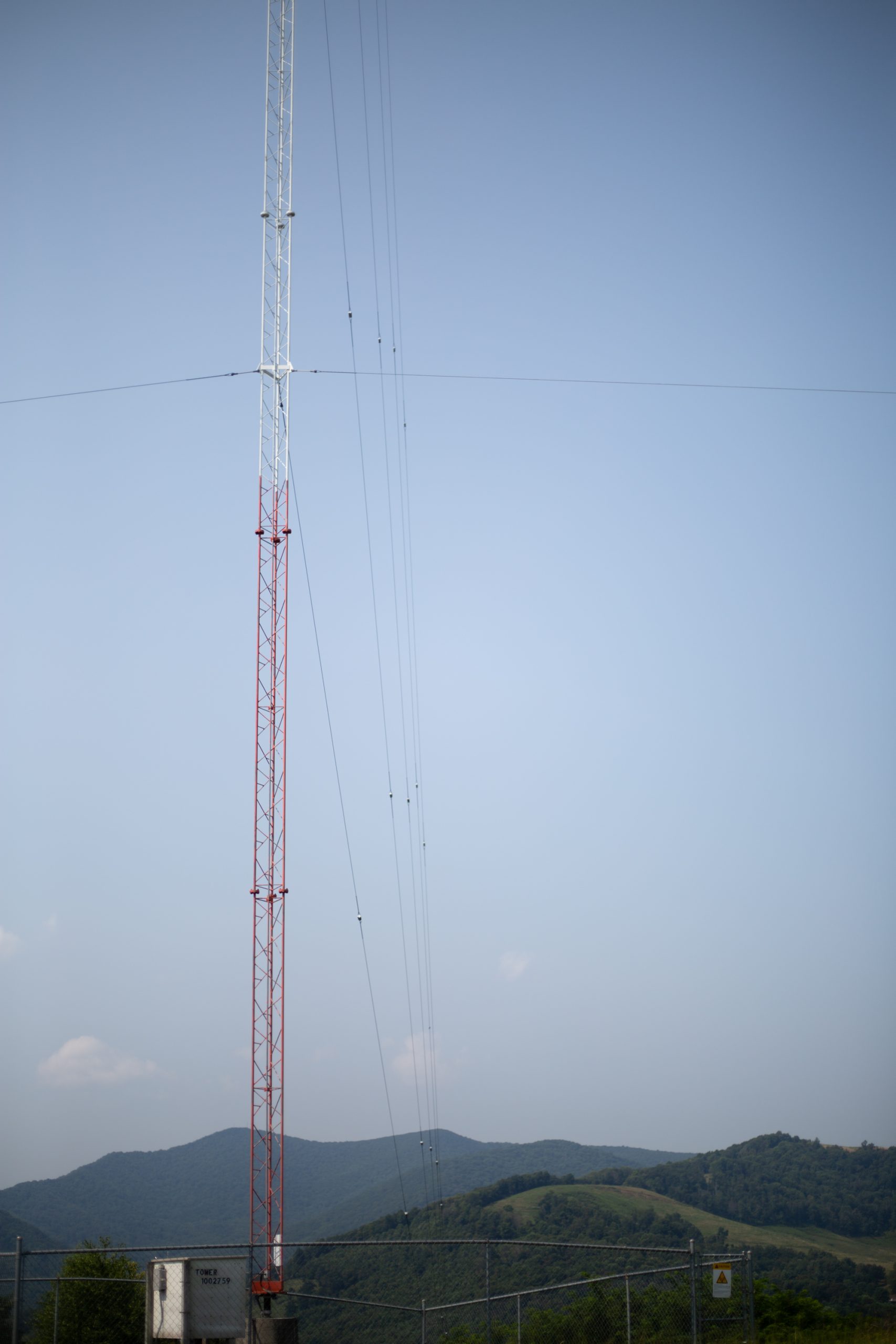 A red and white radio tower rises above mountains