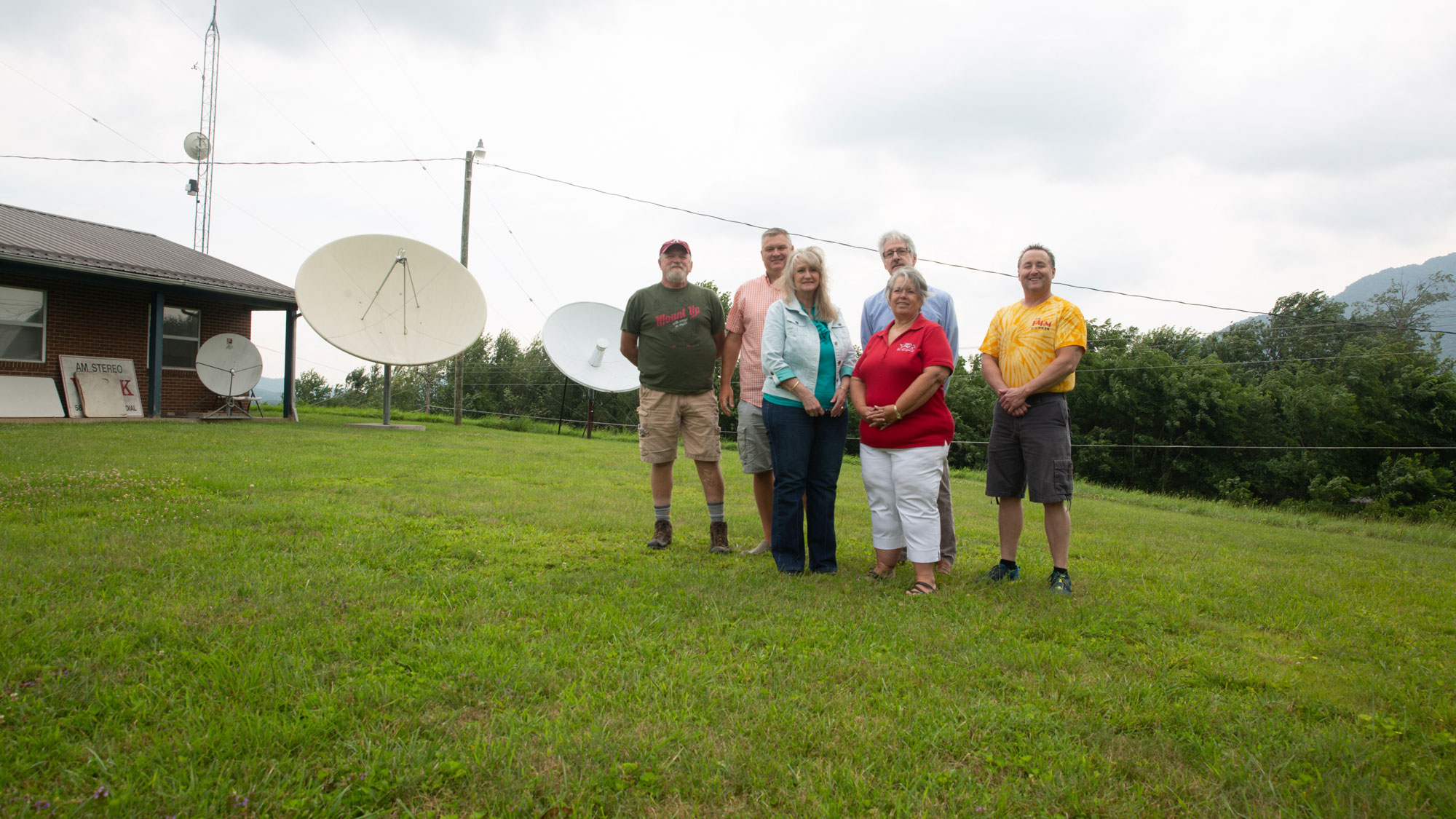 A group of six stands in a field in front of large satellite dishes