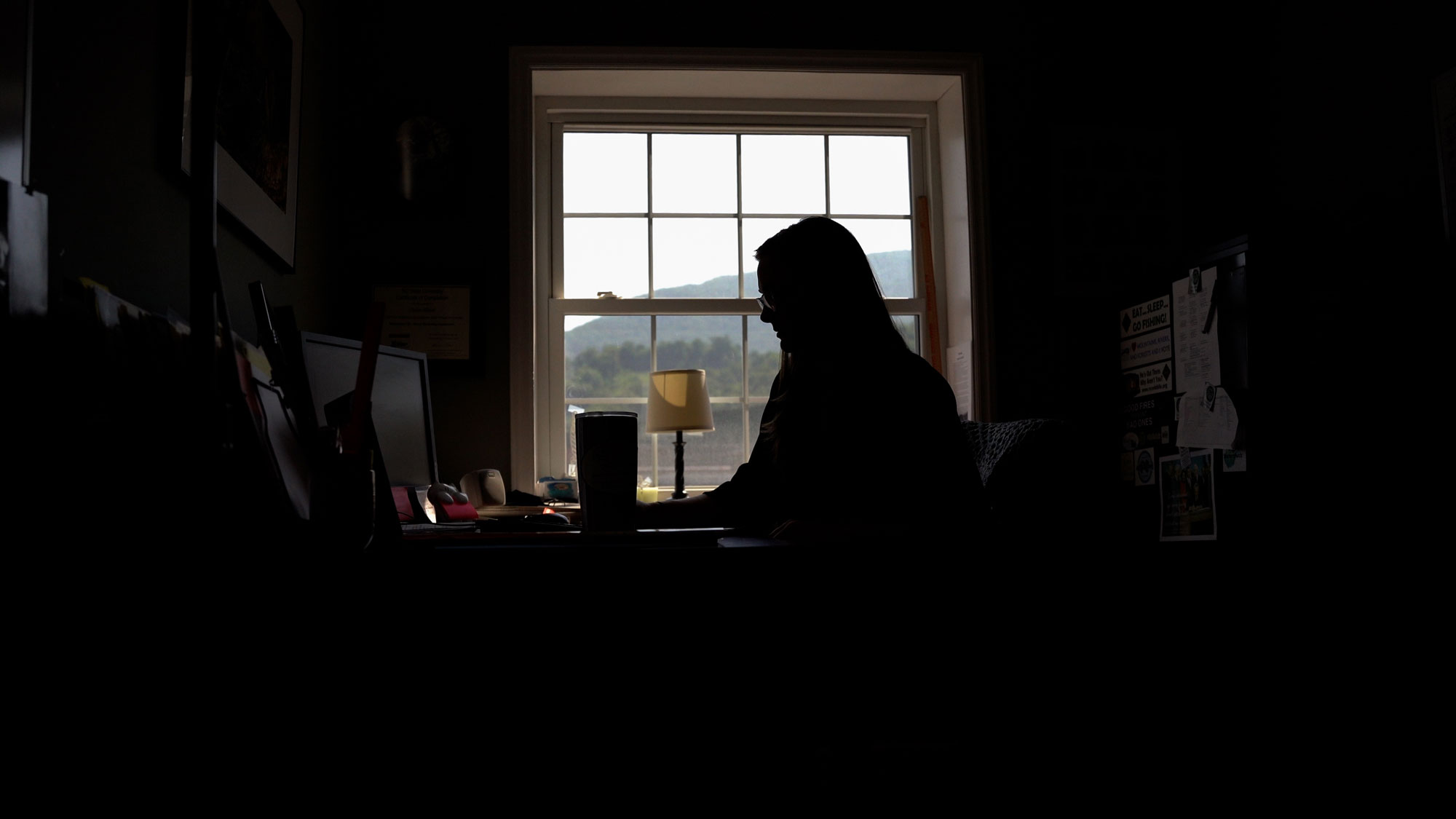 A woman sits in the dark silhouetted against a window