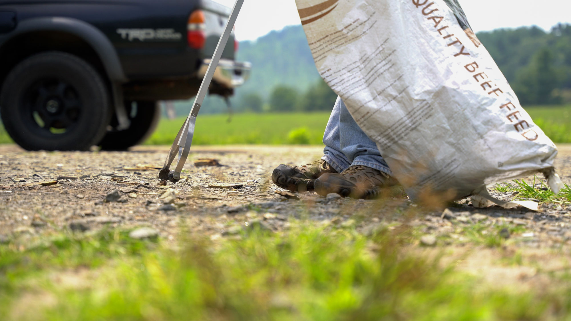 A man's feet stands next to a beef feed bag picking up trash with a grabber