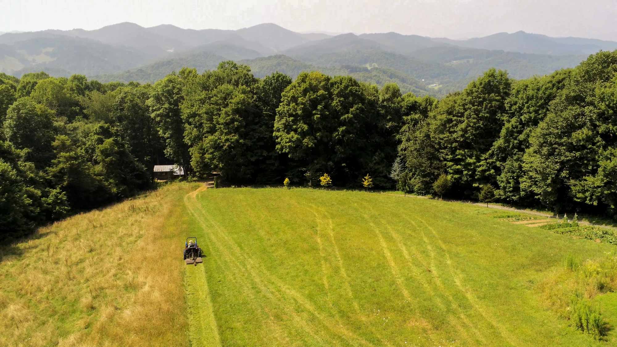 Overhead shot of a riding lawnmower clearing an overgrown field with mountains in the background