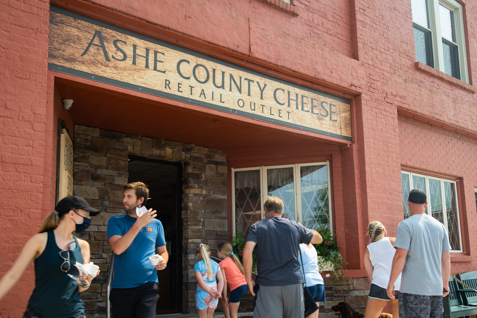 A group of customers flock in and out of a store called "Ashe County Cheese"