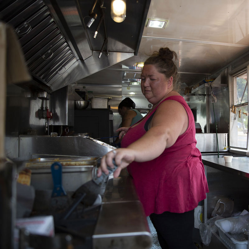 Woman cooking in a food cart reaching over to food