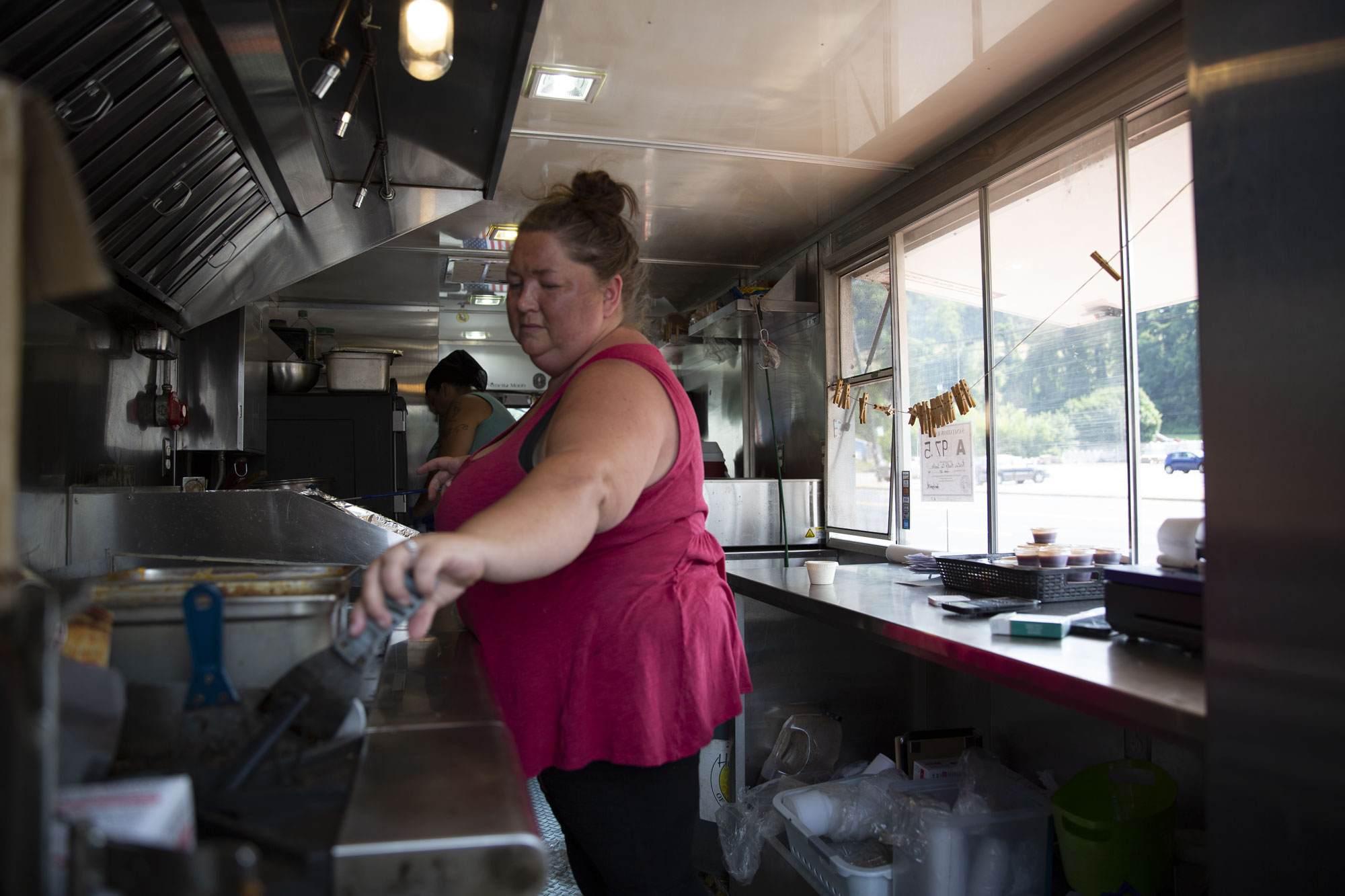 A woman in red reaches for a cooking instrument in a food cart