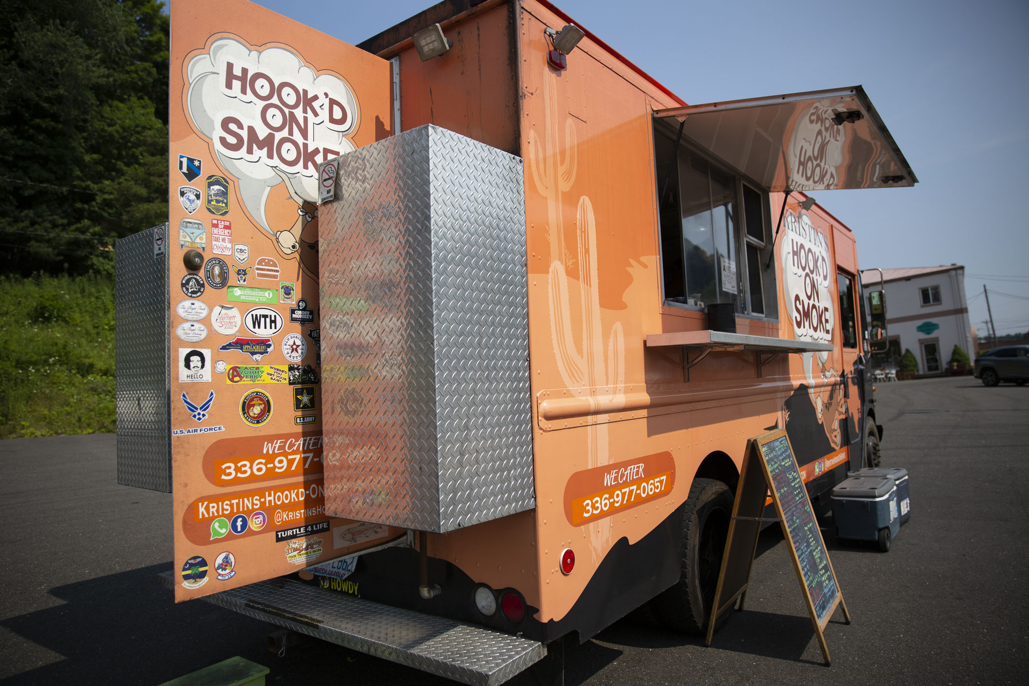 An orange food truck called "Hook'd on Smoke" stands open and ready for business