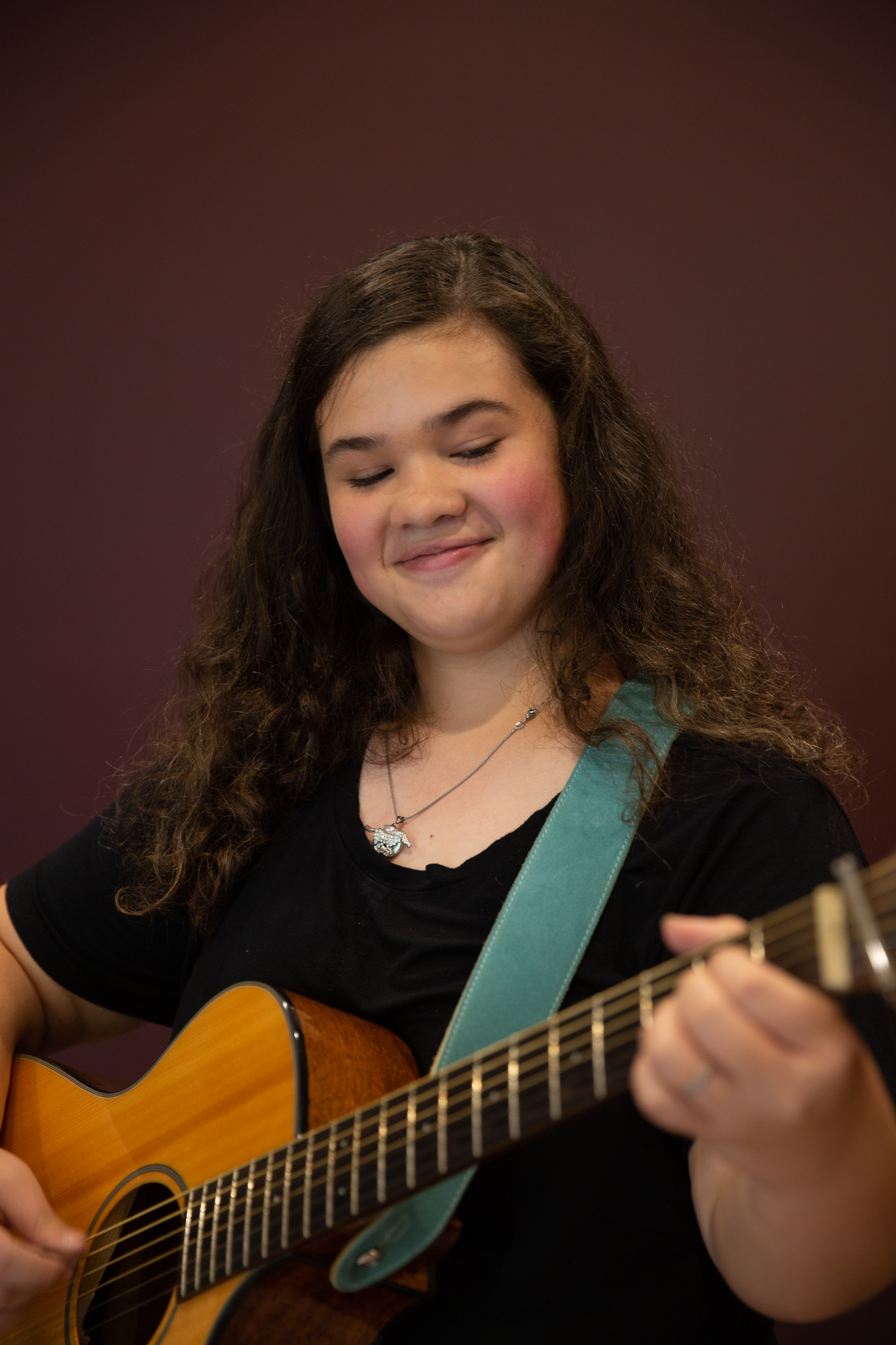 Girl smiles down while playing the guitar