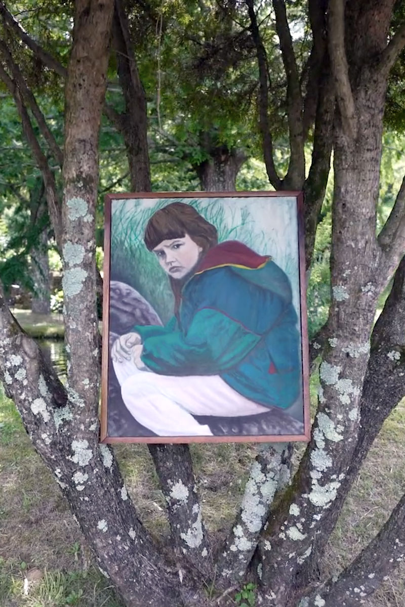 A painting of a girl hunched over in a green jacket sits in the branches of a tree